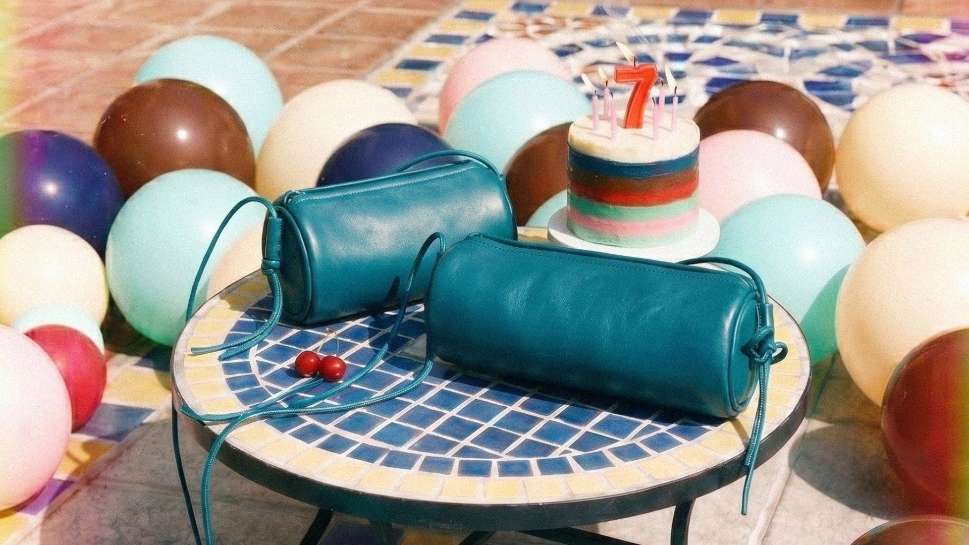 Dos bolsos Alma tubulares de piel de Labienhecha junto a una tarta del 7 aniversario, rodeados de globos